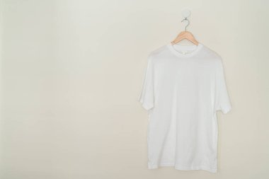 white t-shirt hanging with wood hanger on wall