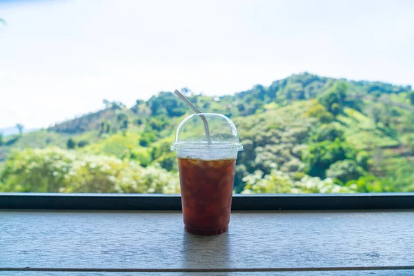 iced black coffee on wood bar with mountain hill background