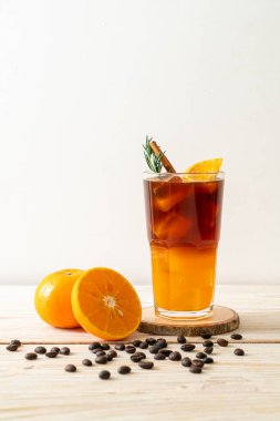 Bir bardak buzlu americano sade kahve ve ahşap arka planda biberiye ve tarçınla süslenmiş portakal ve limon suyu.