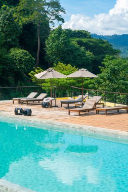 Dağ ve mavi gökyüzü arkaplanlı yüzme havuzunun etrafında şemsiyeli yatak havuzu