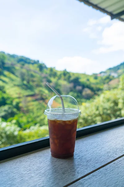 iced black coffee on wood bar with mountain hill background