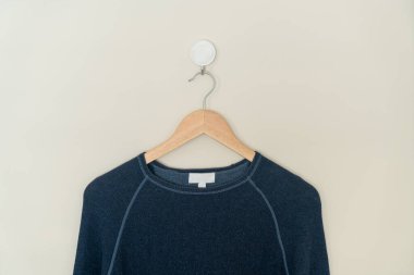 navy sweater hanging with wood hanger on wall