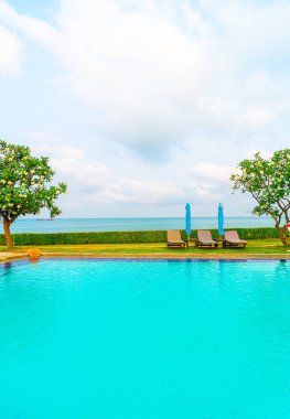 Sandalye havuzu ve şemsiyeyle okyanus arka planında yüzme havuzu