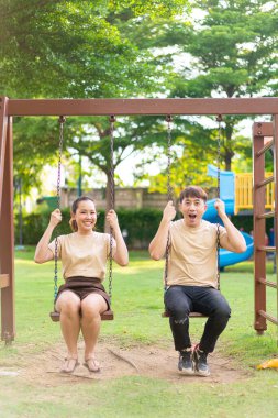 Asian couple love play on the swing in kids playground