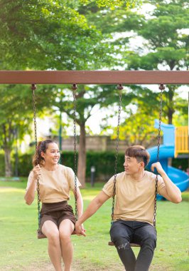 Asian couple love play on the swing in kids playground