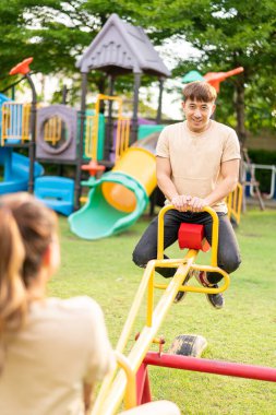 Asian couple love play seesaw with smiling in kids playground