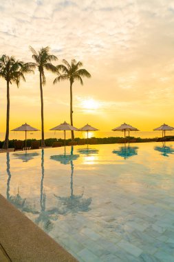 Günbatımında ya da gün doğumunda okyanus arka planında yüzme havuzunun etrafında yüzen şemsiyeli - tatil ve tatil kavramı