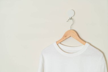 white t-shirt hanging with wood hanger on wall