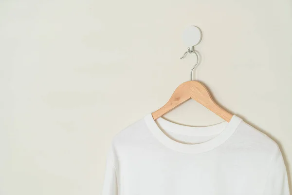 white t-shirt hanging with wood hanger on wall