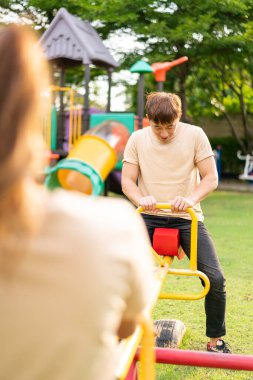 Asian couple love play seesaw with smiling in kids playground
