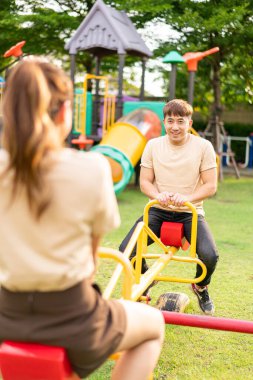 Asian couple love play seesaw with smiling in kids playground