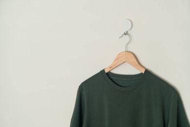 dark green t-shirt hanging with wood hanger on wall