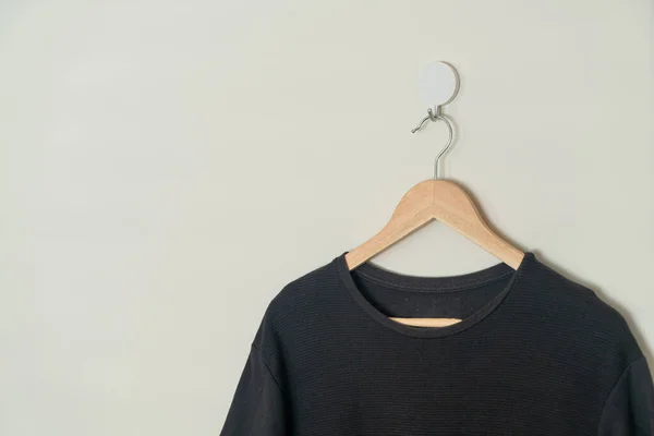 black t-shirt hanging with wood hanger on wall