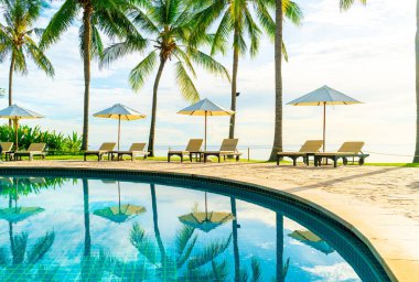 Otelde açık havuzda güzel bir şemsiye ve sandalye ve gün batımında hindistan cevizi palmiyesi ağacı olan bir tatil ve tatil konsepti.