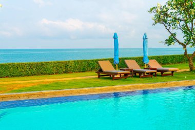 Sandalye havuzu ve şemsiyeyle okyanus arka planında yüzme havuzu