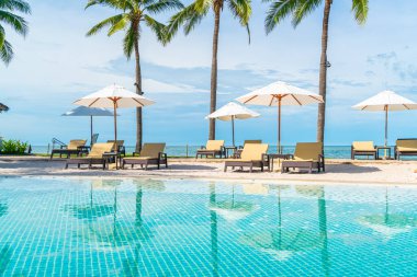 Güzel tropikal plaj ve deniz şemsiyesi ve sandalyesi otel tatil ve tatil için yüzme havuzunda.
