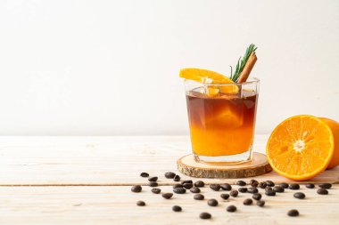 Bir bardak buzlu americano sade kahve ve ahşap arka planda biberiye ve tarçınla süslenmiş portakal ve limon suyu.