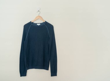 navy sweater hanging with wood hanger on wall