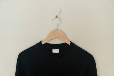 black sweater hanging with wood hanger on wall