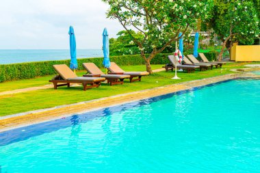 Sandalye havuzu ve şemsiyeyle okyanus arka planında yüzme havuzu