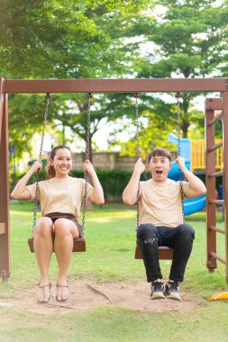 Asian couple love play on the swing in kids playground