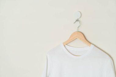 white t-shirt hanging with wood hanger on wall