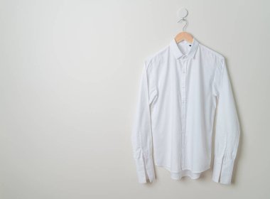 Duvarında ahşap askı olan beyaz gömlek asılı.