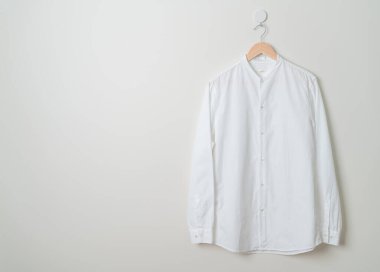 Duvarında ahşap askı olan beyaz gömlek asılı.