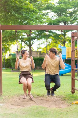 Asian couple love play on the swing in kids playground