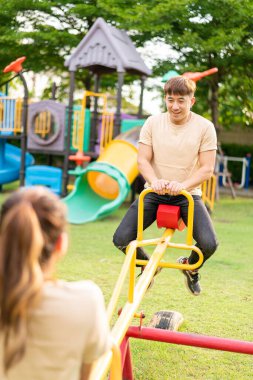 Asian couple love play seesaw with smiling in kids playground