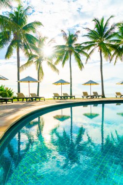 Güzel lüks şemsiye ve sandalye otelin açık havuzu ve mavi gökyüzünde hindistan cevizi palmiyesi ağacı olan bir tatil ve tatil konsepti.