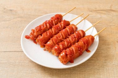 Beyaz tabakta ketçaplı kızarmış sosis şişi.