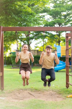 Asian couple love play on the swing in kids playground
