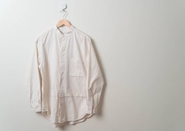 Duvarında ahşap askı olan bej bir gömlek asıyor.