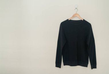 black sweater hanging with wood hanger on wall