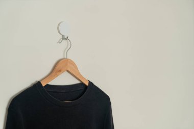 black sweater hanging with wood hanger on wall