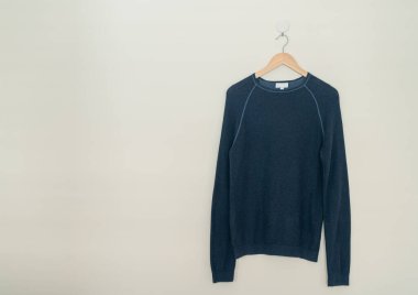 navy sweater hanging with wood hanger on wall