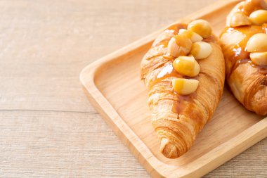 Macadamia ve ahşap tabakta karamel ile kruvasan.
