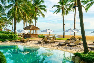 Otelde açık havuzda güzel bir şemsiye ve sandalye ve gün batımında hindistan cevizi palmiyesi ağacı olan bir tatil ve tatil konsepti.