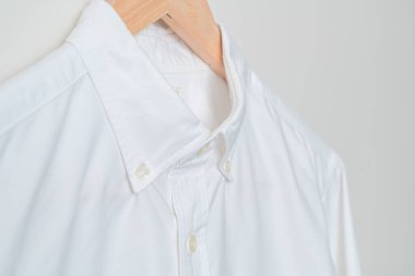 Duvarında ahşap askı olan beyaz gömlek asılı.