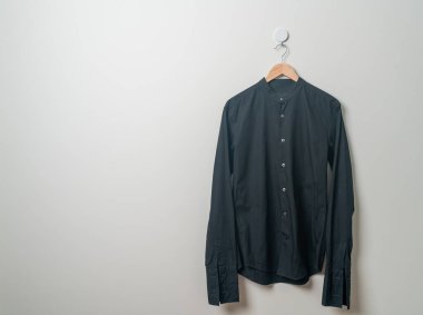 Duvarında ahşap askı olan siyah bir gömlek asıyor.