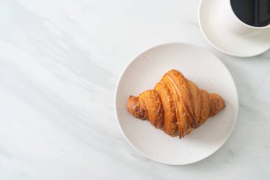 Beyaz tabakta taze kruvasan ve siyah kahve.