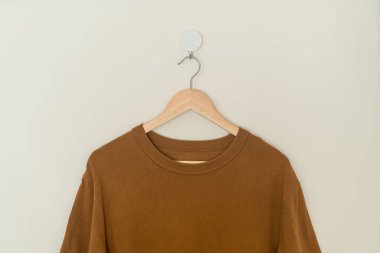 brown t-shirt hanging with wood hanger on wall