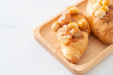 Macadamia ve ahşap tabakta karamel ile kruvasan.