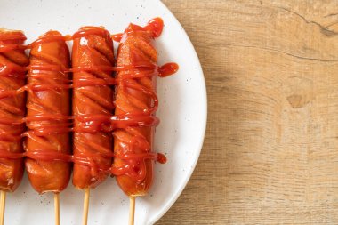 Beyaz tabakta ketçaplı kızarmış sosis şişi.