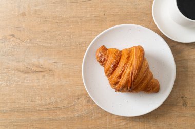 Beyaz tabakta taze kruvasan ve siyah kahve.