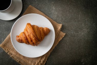 Beyaz tabakta taze kruvasan ve siyah kahve.