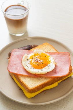 Ev yapımı ekmek üzerine kızarmış peynir jambon ve kızarmış yumurta ile domuz sosisi ve kahvaltıda kahve.