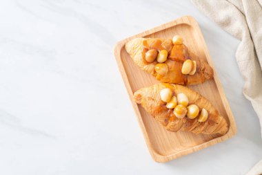 Macadamia ve ahşap tabakta karamel ile kruvasan.