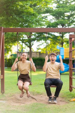 Asian couple love play on the swing in kids playground